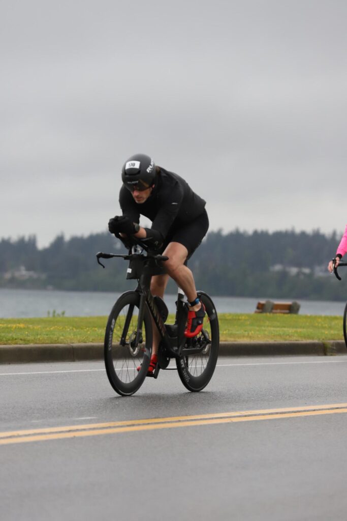 Jay riding a time trial bike along a lakeside road